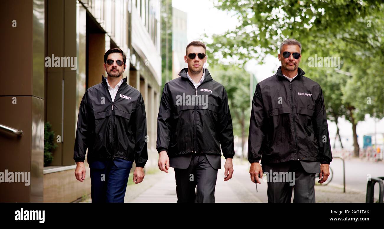 un gruppo di agenti di sicurezza pattuglia le strade, salvaguardando gli edifici e controllando la sorveglianza con i loro walkie-talkie. Foto Stock