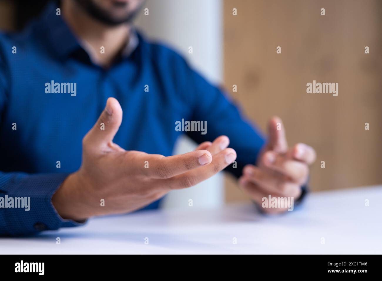 Gesti con le mani, uomo in camicia blu che parla di affari al tavolo dell'ufficio, copia spazio Foto Stock