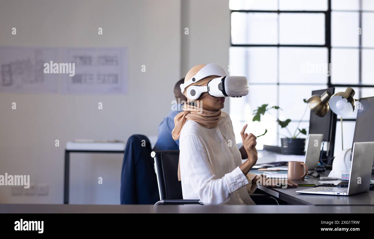 Utilizzando il visore VR, una donna che lavora alla scrivania in un ufficio moderno, copia spazio Foto Stock