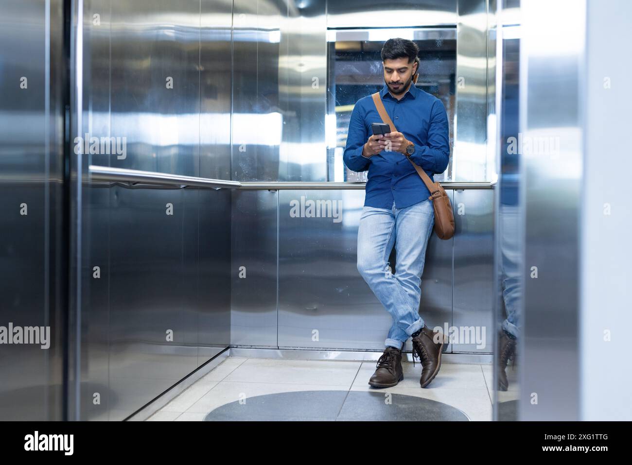 Utilizzando lo smartphone, l'uomo in piedi in ascensore, indossando abbigliamento casual da lavoro, spazio fotocopie Foto Stock