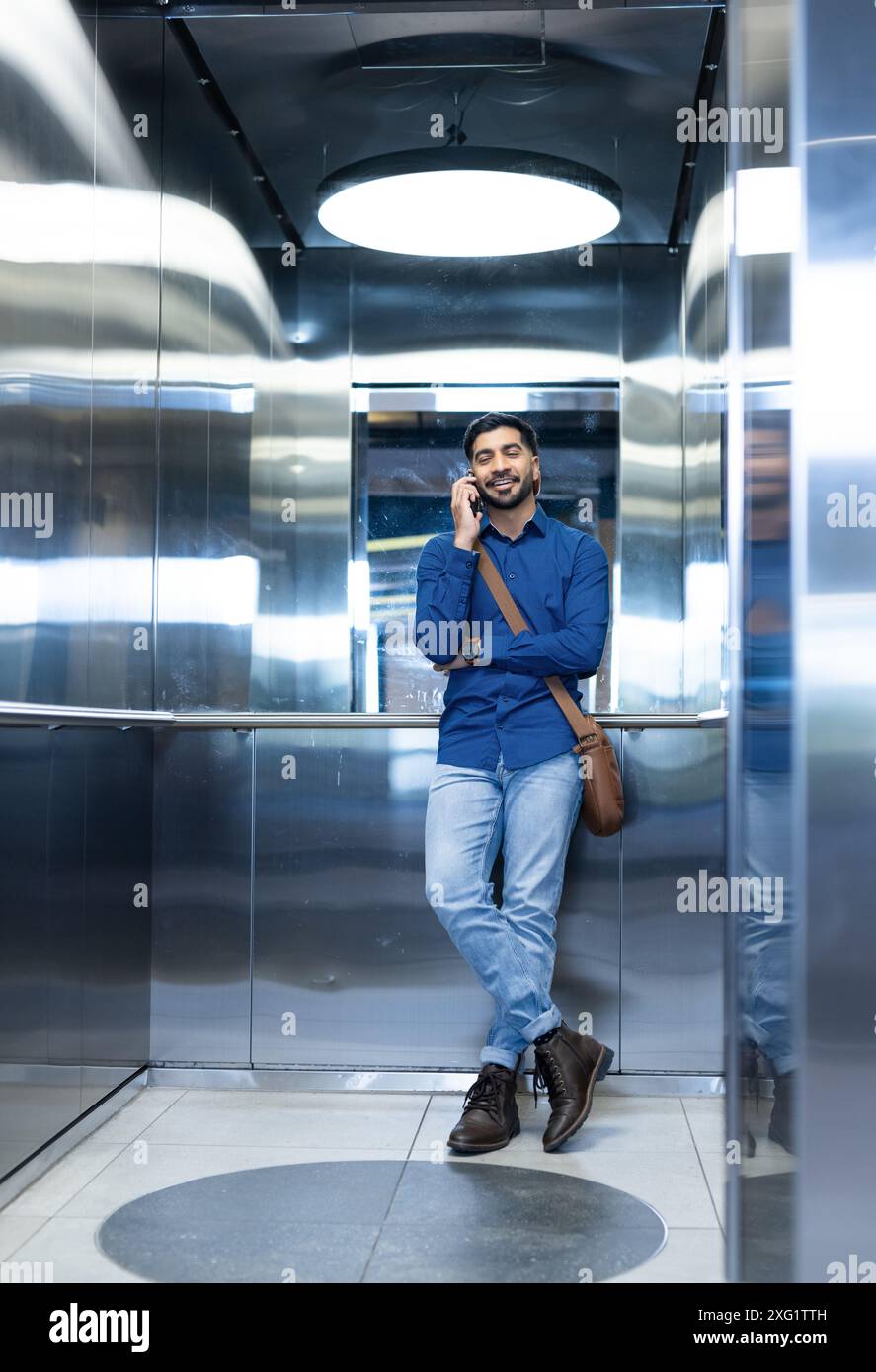Parla con lo smartphone, uomo in un abbigliamento informale in piedi in ascensore Foto Stock