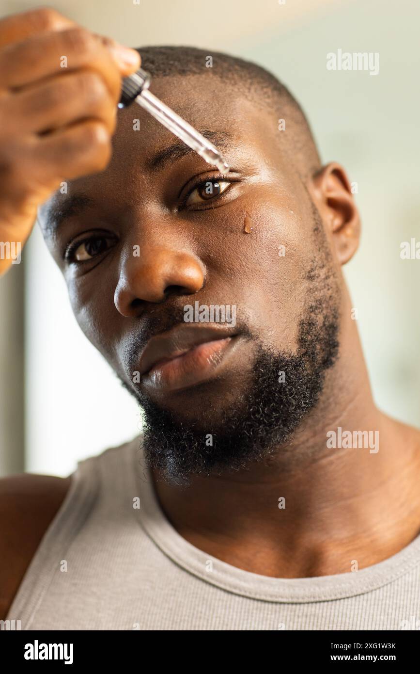 Applicando siero facciale, uomo che si concentra sulla routine della cura della pelle a casa Foto Stock