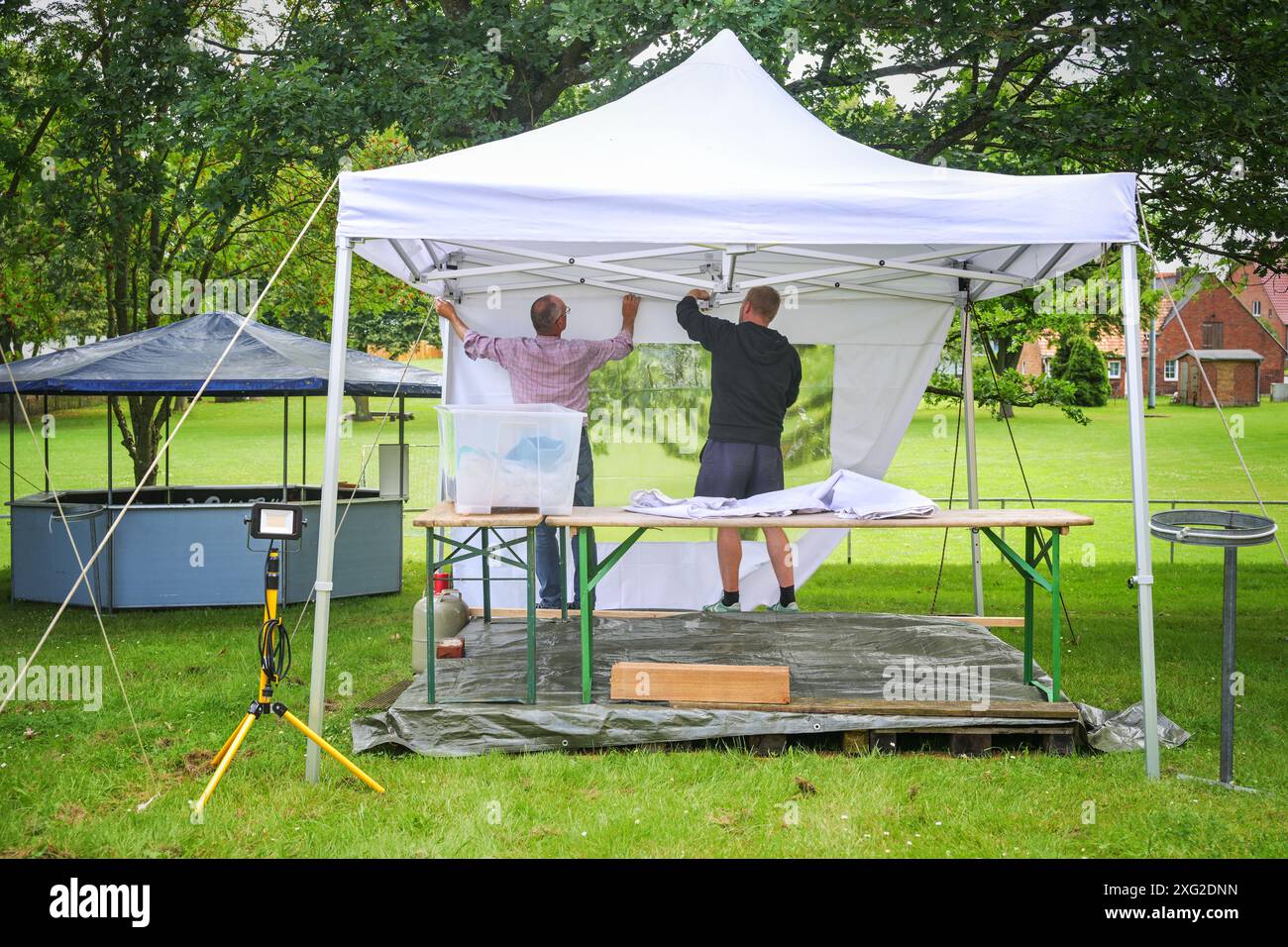 Due uomini alle spalle allestiscono un padiglione per feste per un festival estivo sul prato di un parco, selezionato Foto Stock