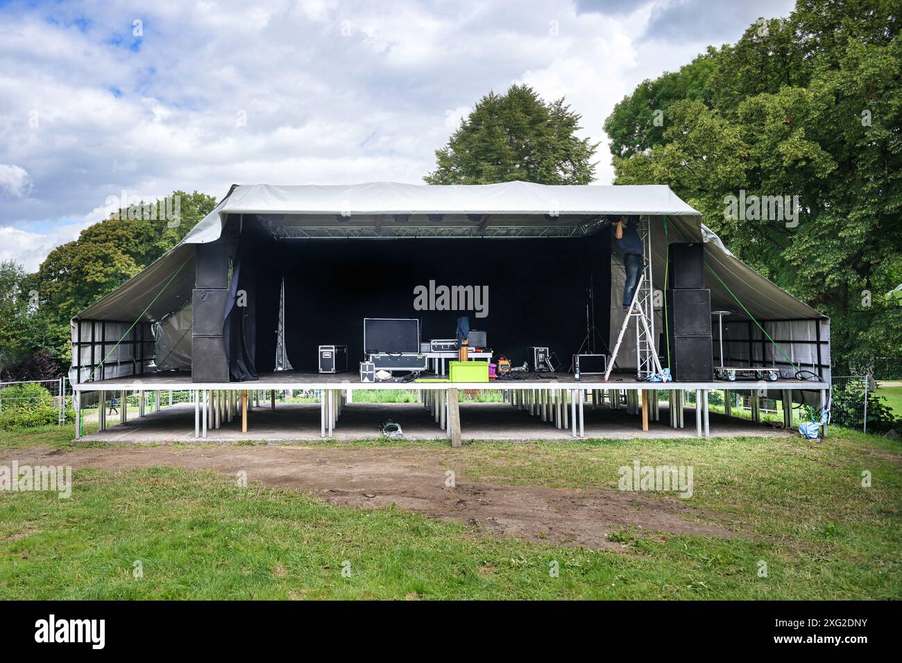 Il palcoscenico all'aperto è allestito con piattaforme, teli per tetti, capriate luminose e apparecchiature audio per un festival musicale all'aperto di campagna sul prato i. Foto Stock
