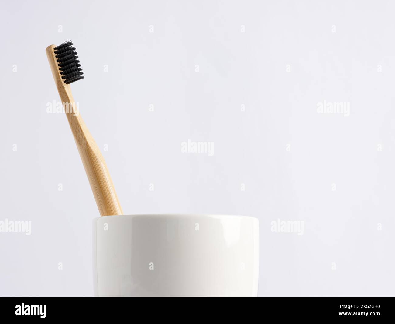 Primo piano di uno spazzolino in bambù in una tazza bianca su sfondo bianco. Concetto di igiene dentale e cura dei denti. Foto Stock