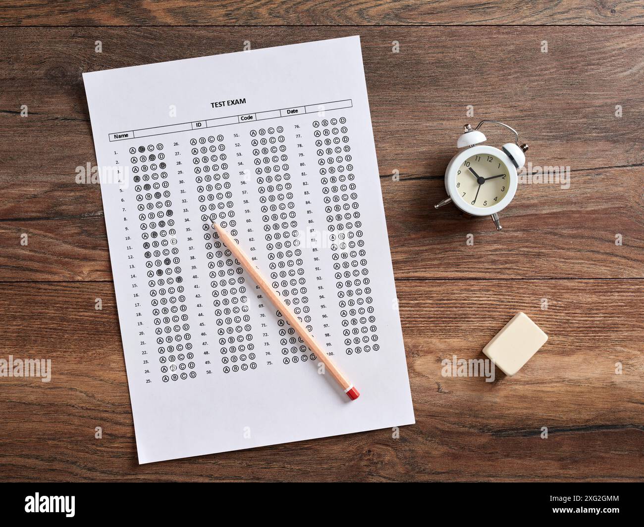 Vista dall'alto di una carta per esami con sveglia, matita e gomma su una scrivania in legno. Formazione e gestione del tempo in esami, quiz e scuola Foto Stock