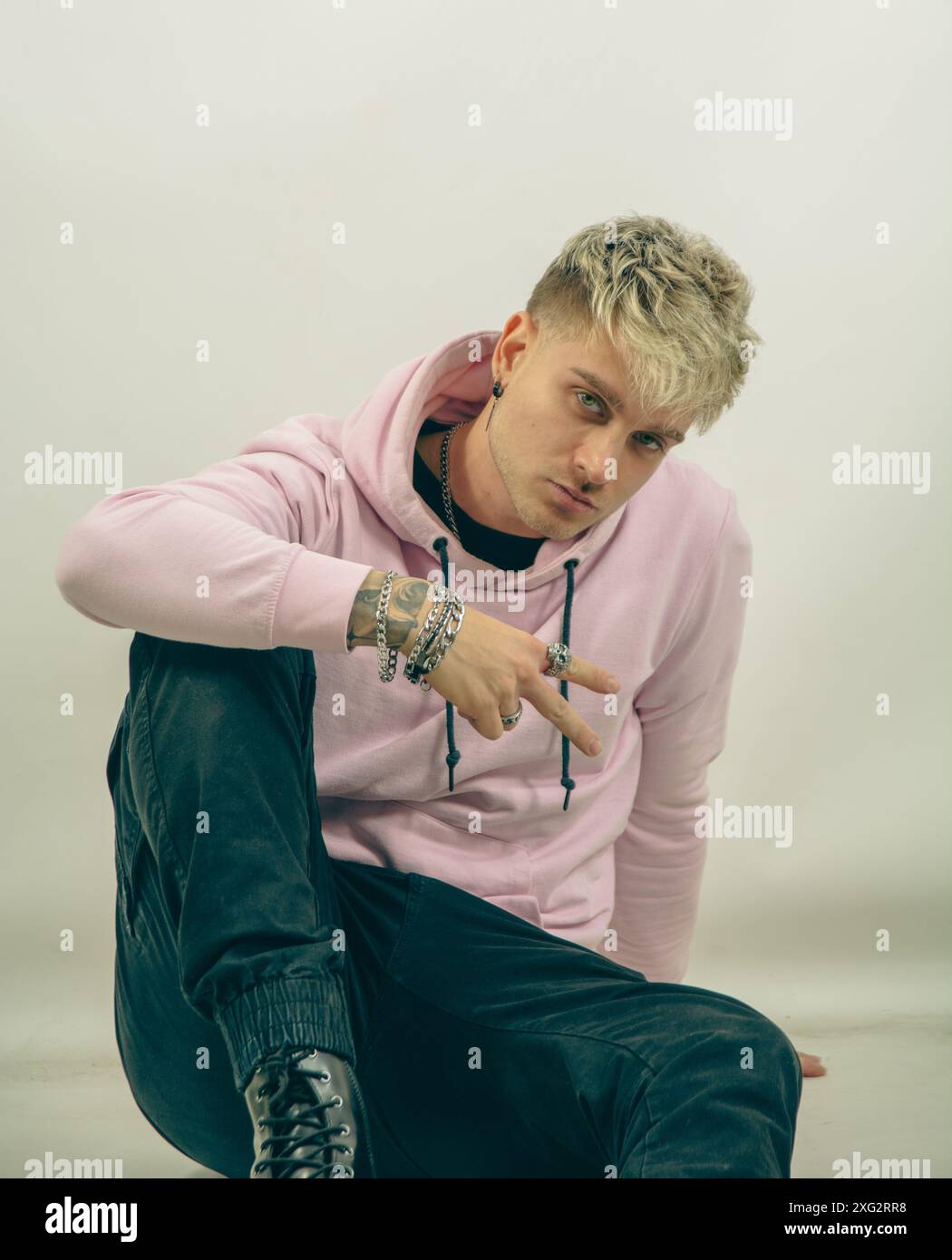 Un uomo che indossa una felpa con cappuccio rosa sta facendo il segno V per la vittoria con la sua mano. Il suo braccio è esteso, e sembra che stia dirigendo l'attenzione verso un oggetto o direzione specifici. Foto Stock