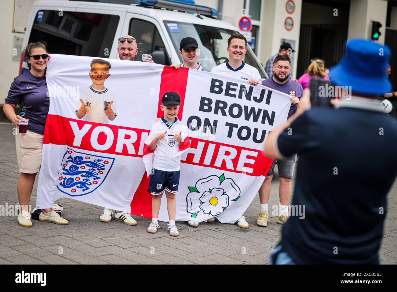 Duesseldorf, Germania. 6 luglio 2024. Calcio: Campionato europeo, Inghilterra - Svizzera, finale, quarto di finale: I tifosi inglesi scattano una foto ricordo con uno striscione davanti a un'auto della polizia nella città vecchia. Crediti: Christoph Reichwein/dpa/Alamy Live News Foto Stock