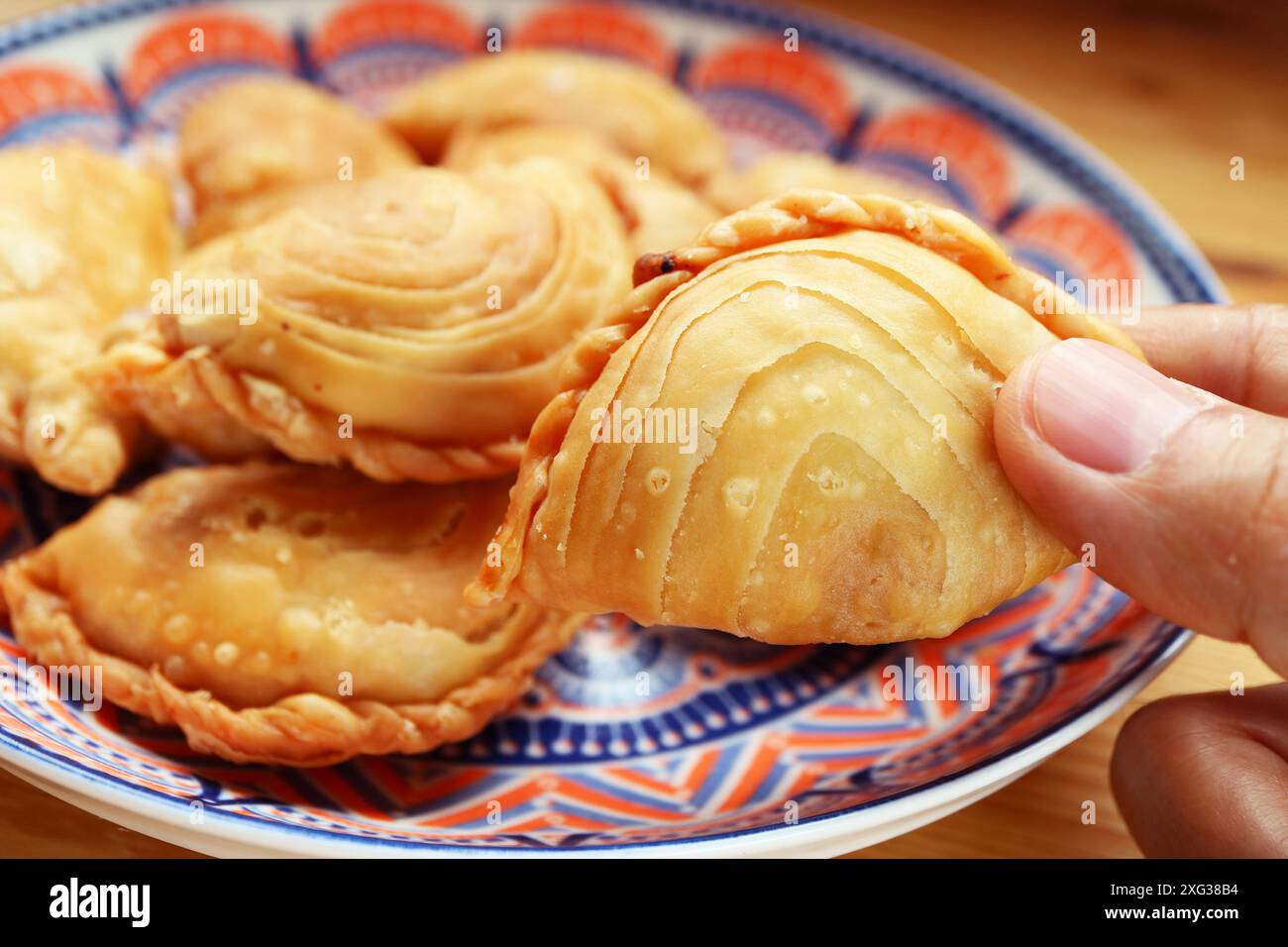 Primo piano di Hand picking a Thai Curry Puff, popolare spuntino simile a Empanadas e Samosa Foto Stock