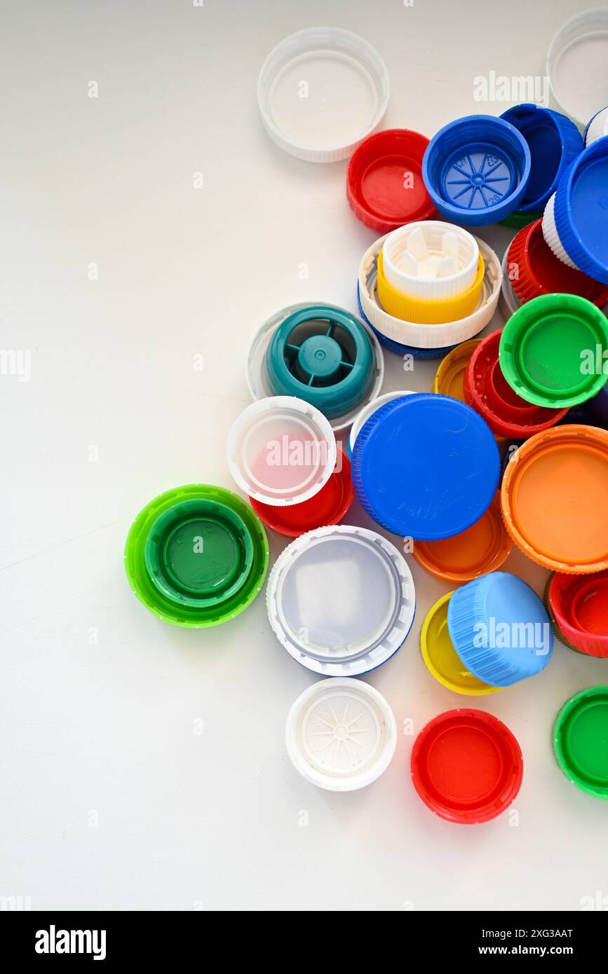 Foto con alcuni cappucci multicolore di bottiglie di plastica giacciono su un tavolo bianco in ordine caotico Foto Stock