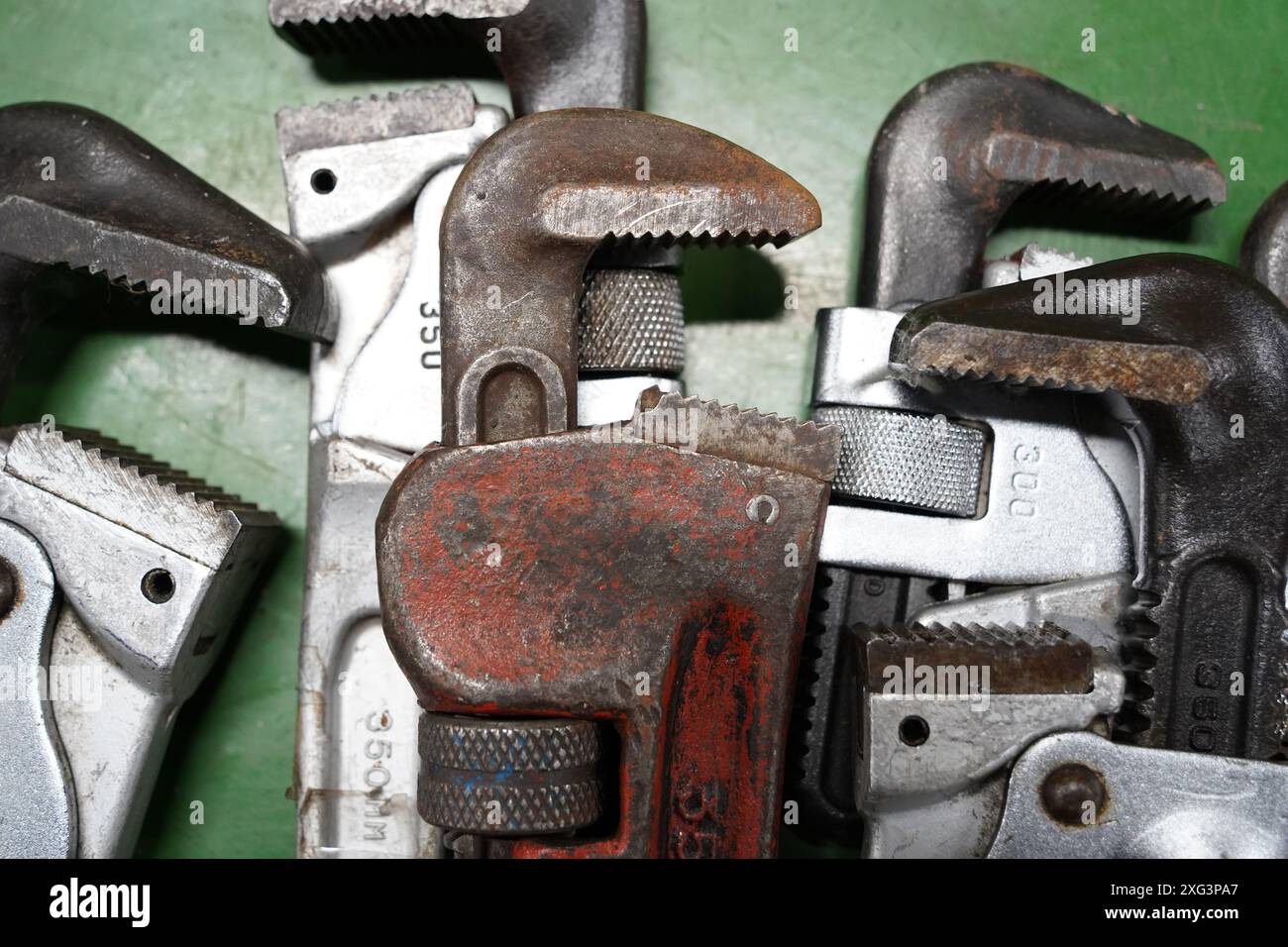 Vecchia chiave per tubi arrugginita e altri utensili su sfondo verde, primo piano Foto Stock