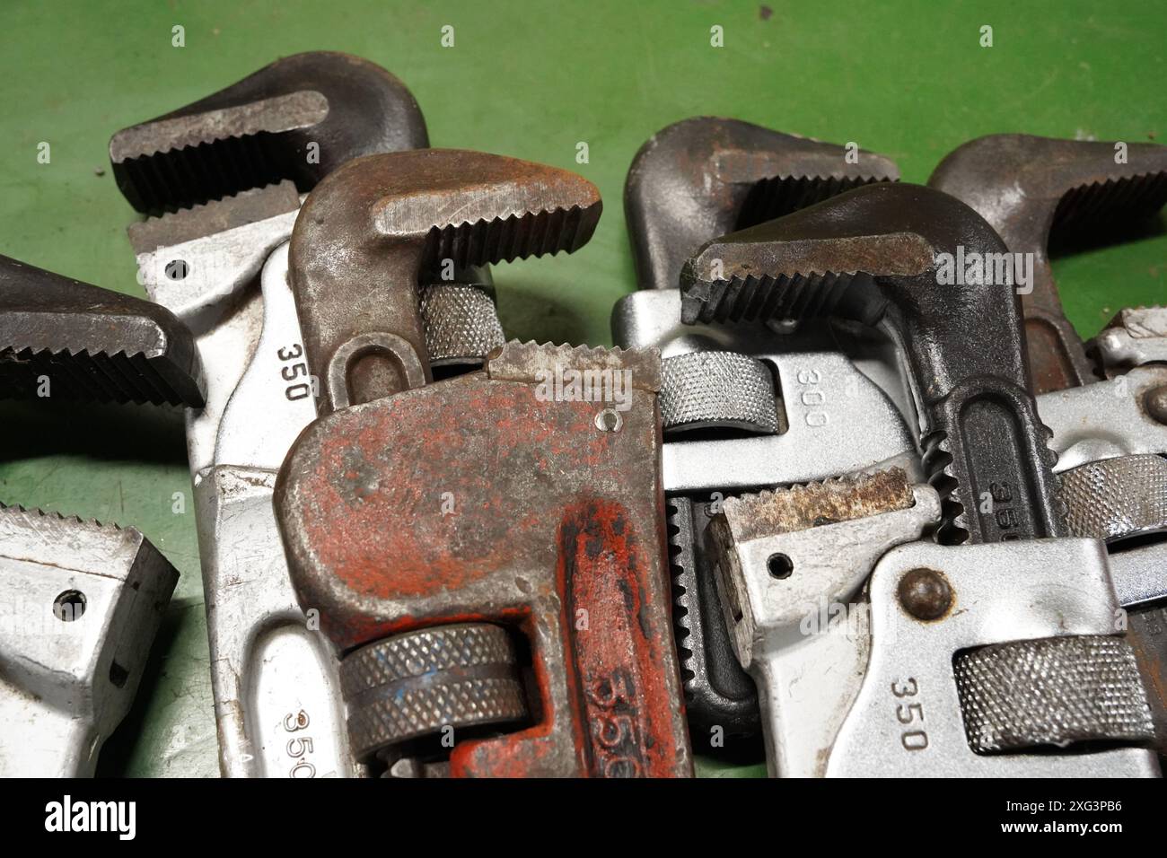 Vecchia chiave per tubi arrugginita e altri utensili su sfondo verde, primo piano Foto Stock