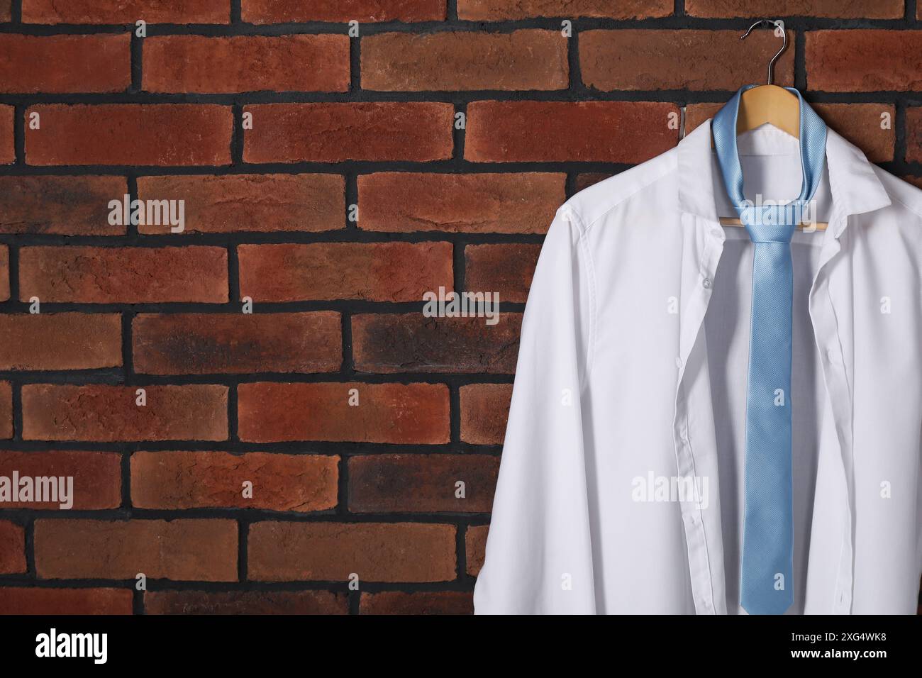 Appendiabiti con camicia bianca e cravatta azzurra sulla parete in mattoni rossi. Spazio per il testo Foto Stock
