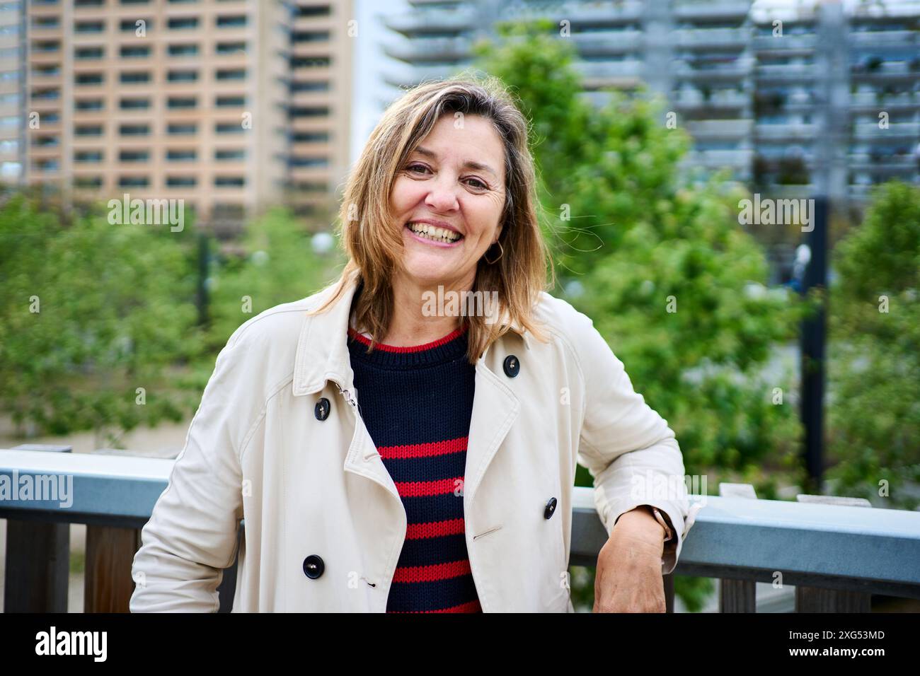 Ritratto di una donna bionda caucasica matura e gioiosa che posa felice in piedi appoggiata su ringhiere all'aperto. Foto Stock