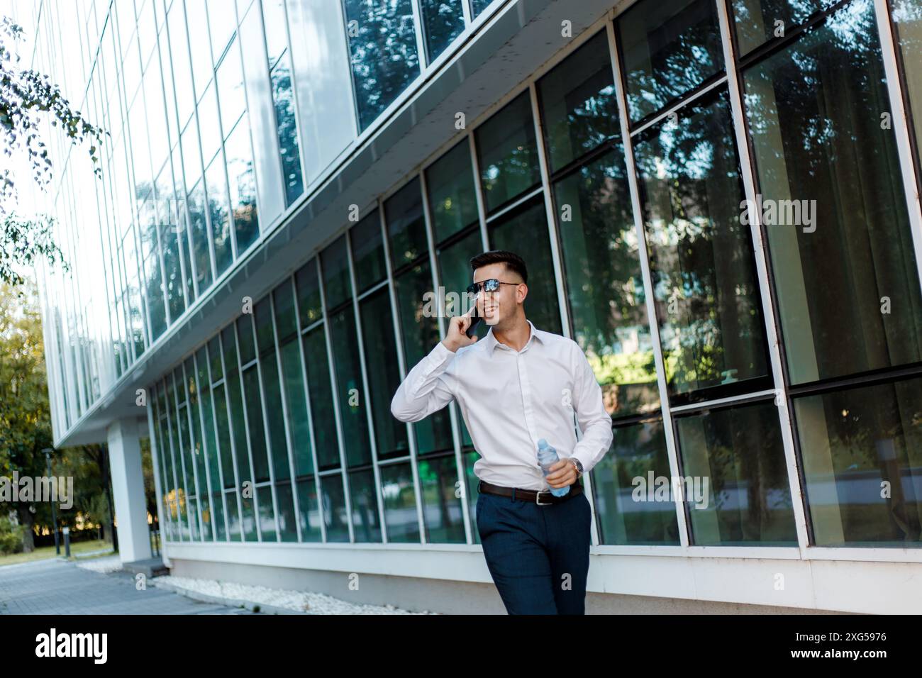 Un uomo che indossa una camicia bianca e pantaloni blu è impegnato in una conversazione telefonica. Foto Stock