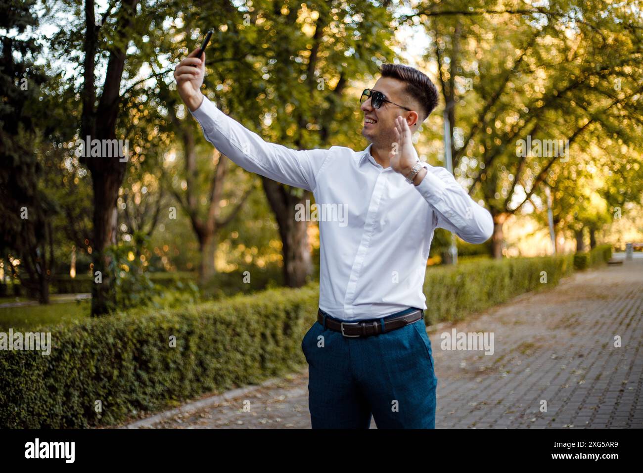 Un uomo che indossa una camicia bianca e pantaloni blu tiene in mano un cellulare. Foto Stock