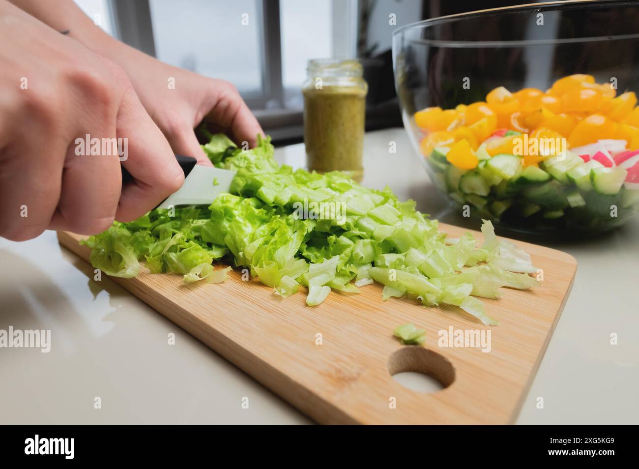 Primo piano della mano di una ragazza tagliare un'insalata su un tavolo di legno, una donna prepara un'insalata vegetariana, cibo sano, un coltello taglia le verdure Foto Stock