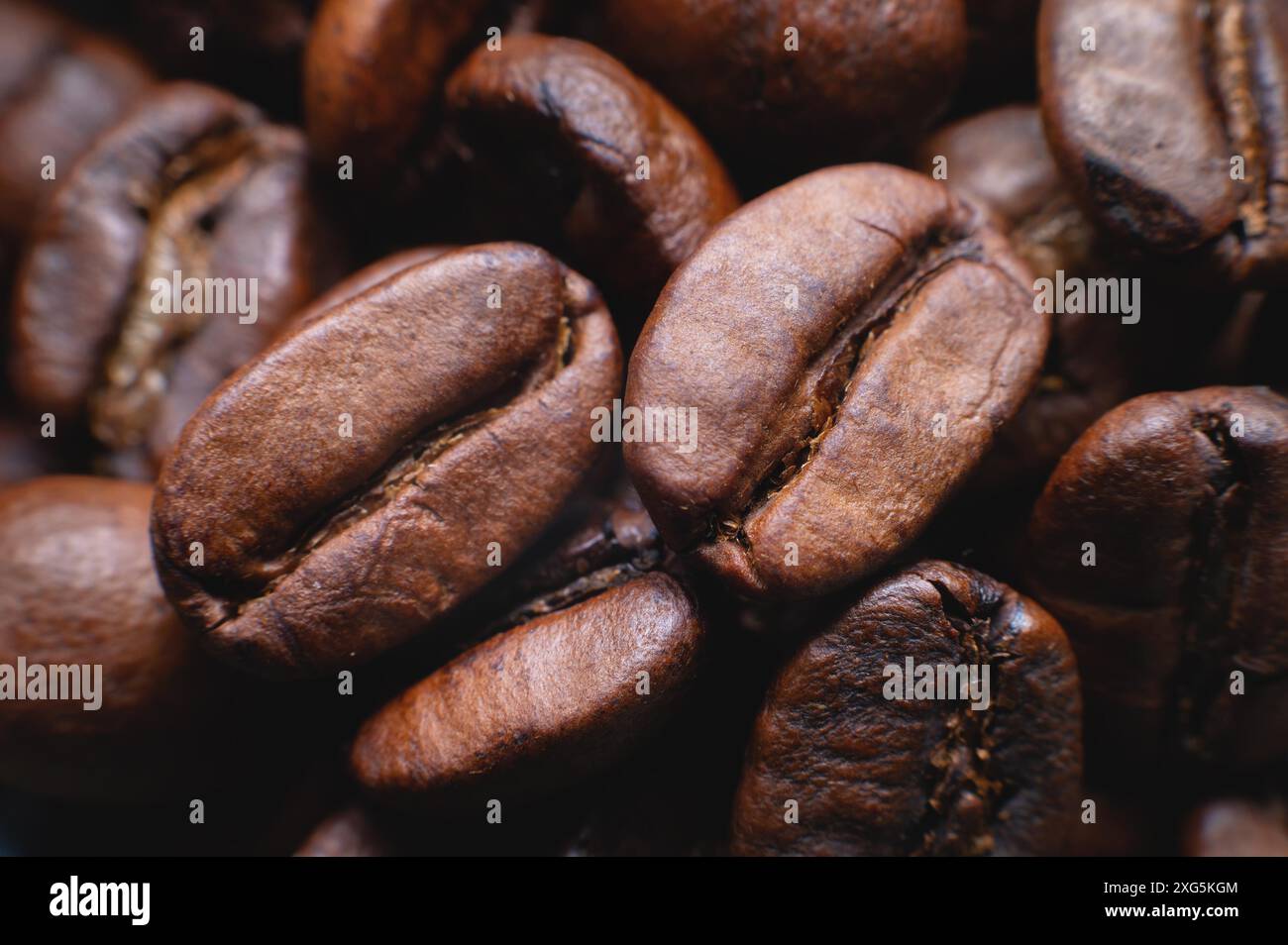 Primo piano su un gruppo macro estremo di chicchi di caffè tostati di colore marrone o nero con una profondità di campo ridotta. Delizioso aroma di caffè Foto Stock