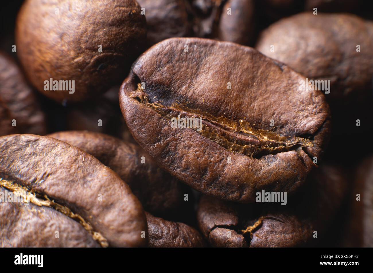 Primo piano su un gruppo macro estremo di chicchi di caffè tostati di colore marrone o nero con una profondità di campo ridotta. Delizioso aroma di caffè Foto Stock