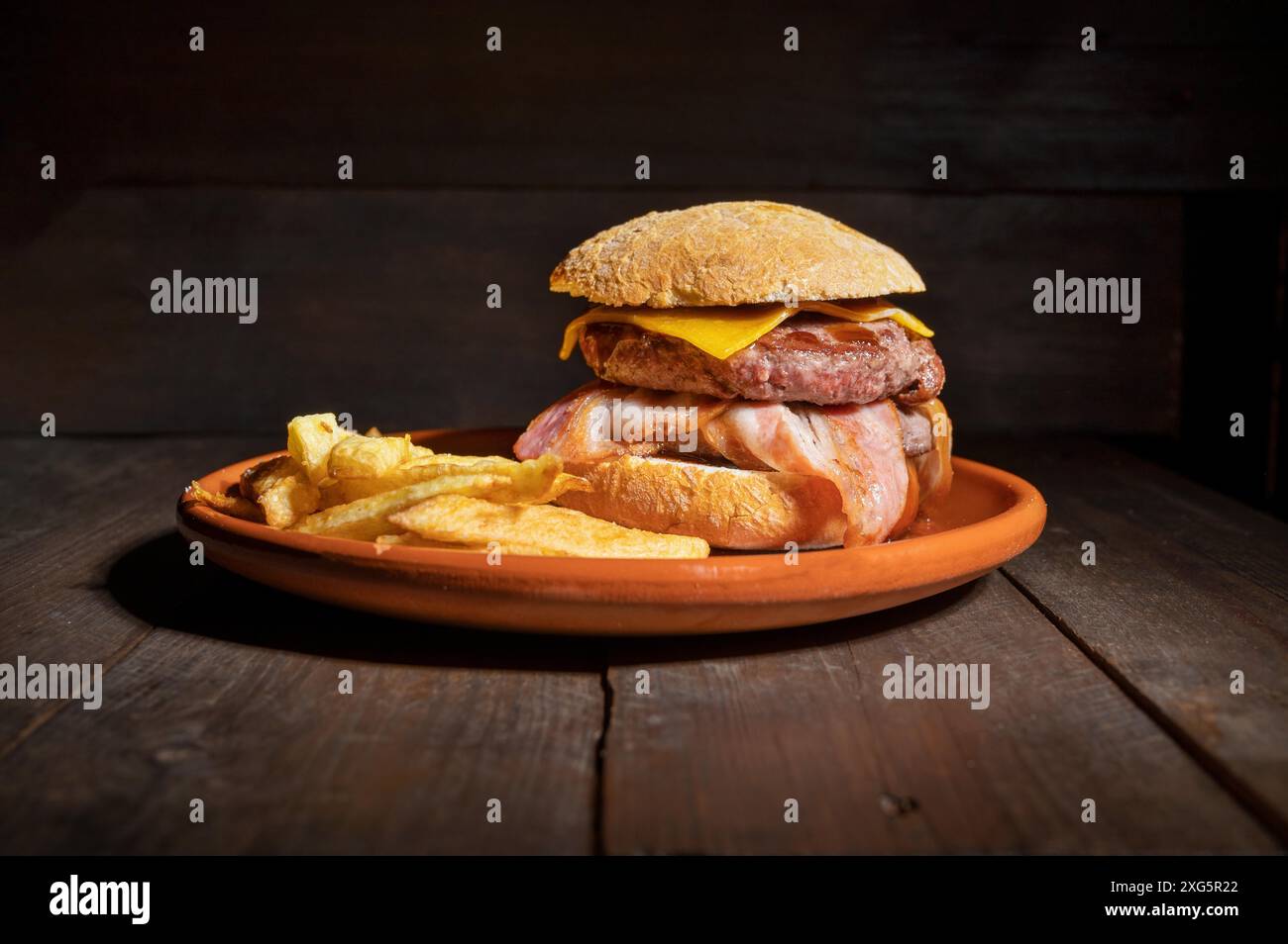 Hamburger di manzo alla griglia di prima qualità con pancetta, formaggio e patatine fritte. Delizioso hamburger americano su sfondo di legno. Fotografia di alta qualità Foto Stock