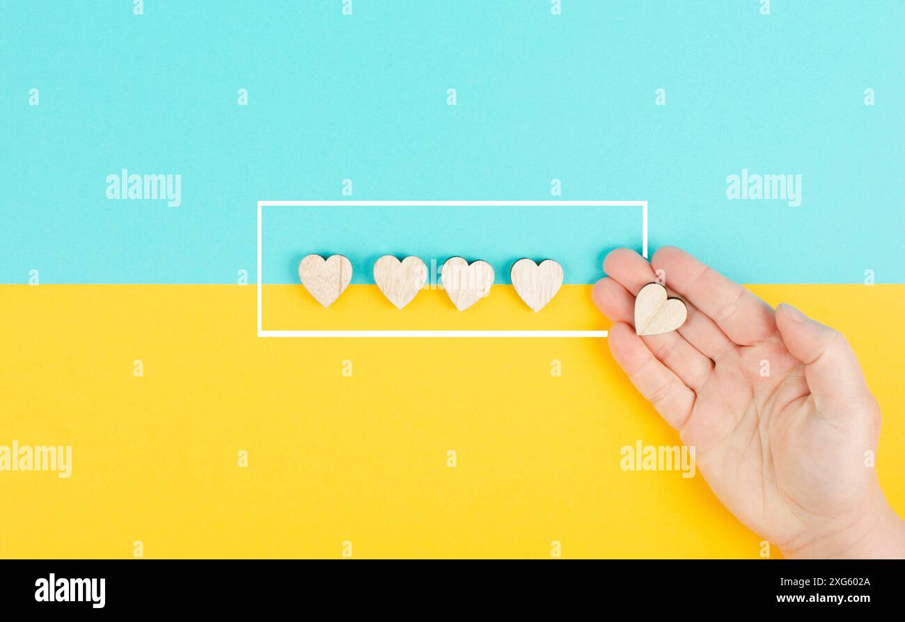 Cinque cuori su uno sfondo blu e giallo, mano mettere l'ultimo cuore in fila, valutare, dare feedback, valutazione aziendale Foto Stock