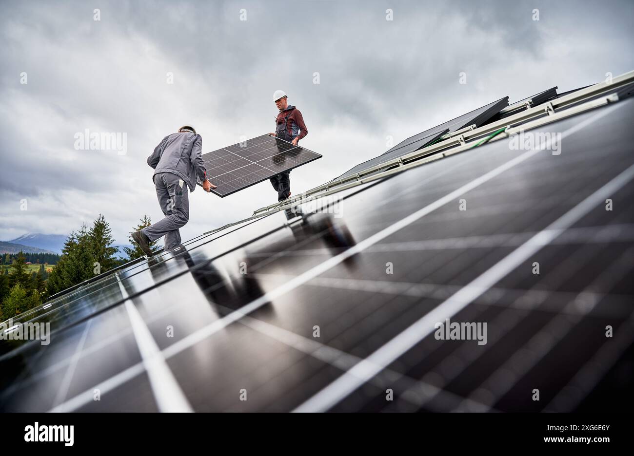 Lavoratori che installano batterie solari su un tetto di casa. Ingegneri maschi che trasportano pannelli fotovoltaici. Concetto di risorse energetiche verdi. Foto Stock