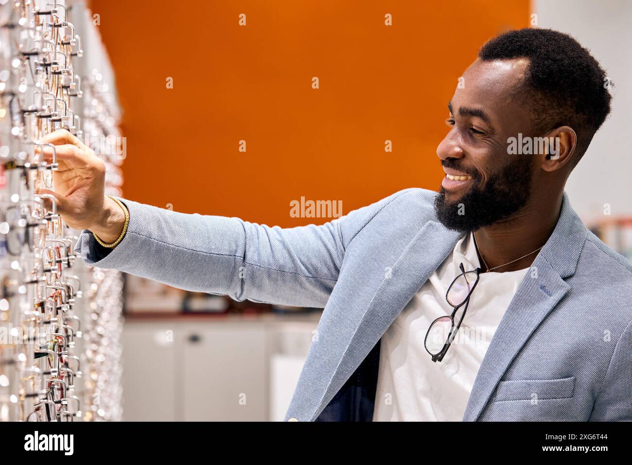 uomo piacevole e bello con un sorriso in faccia che sceglie gli occhiali in un negozio di ottica, foto da vicino. lavoro, professione, occupazione Foto Stock