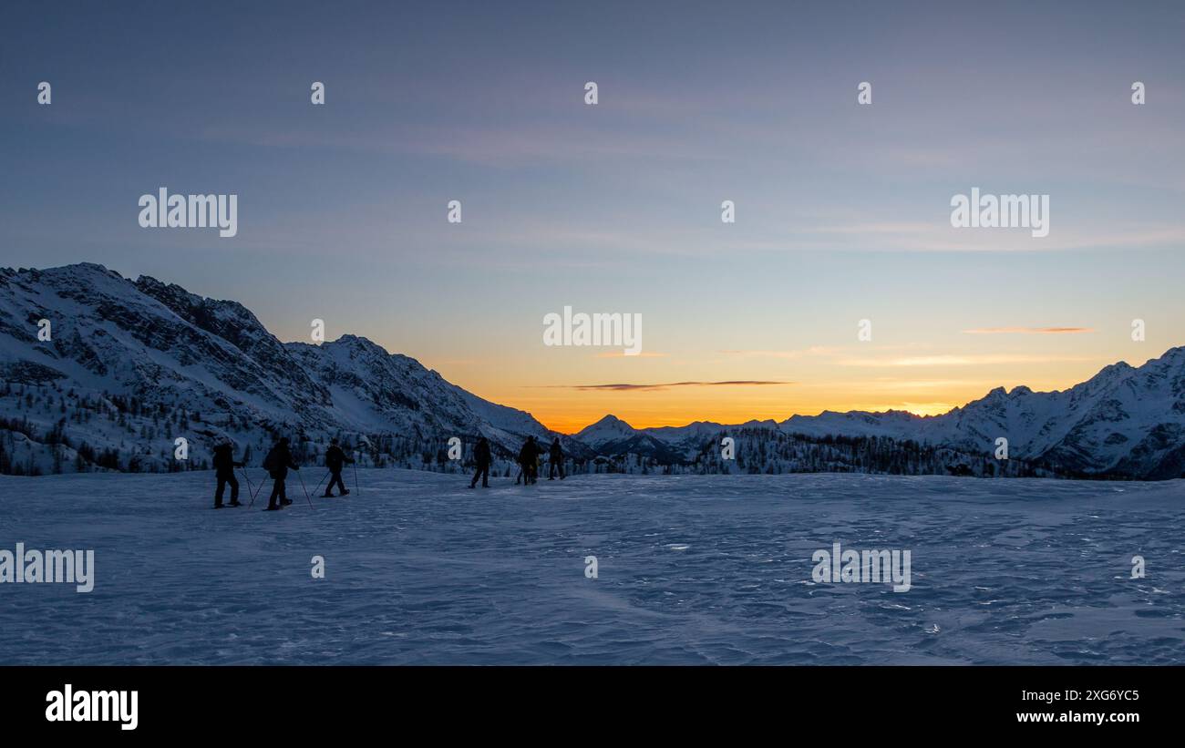 vista panoramica della vallata innevata al tramonto, un gruppo di ciaspole che camminano sulla neve. Foto Stock