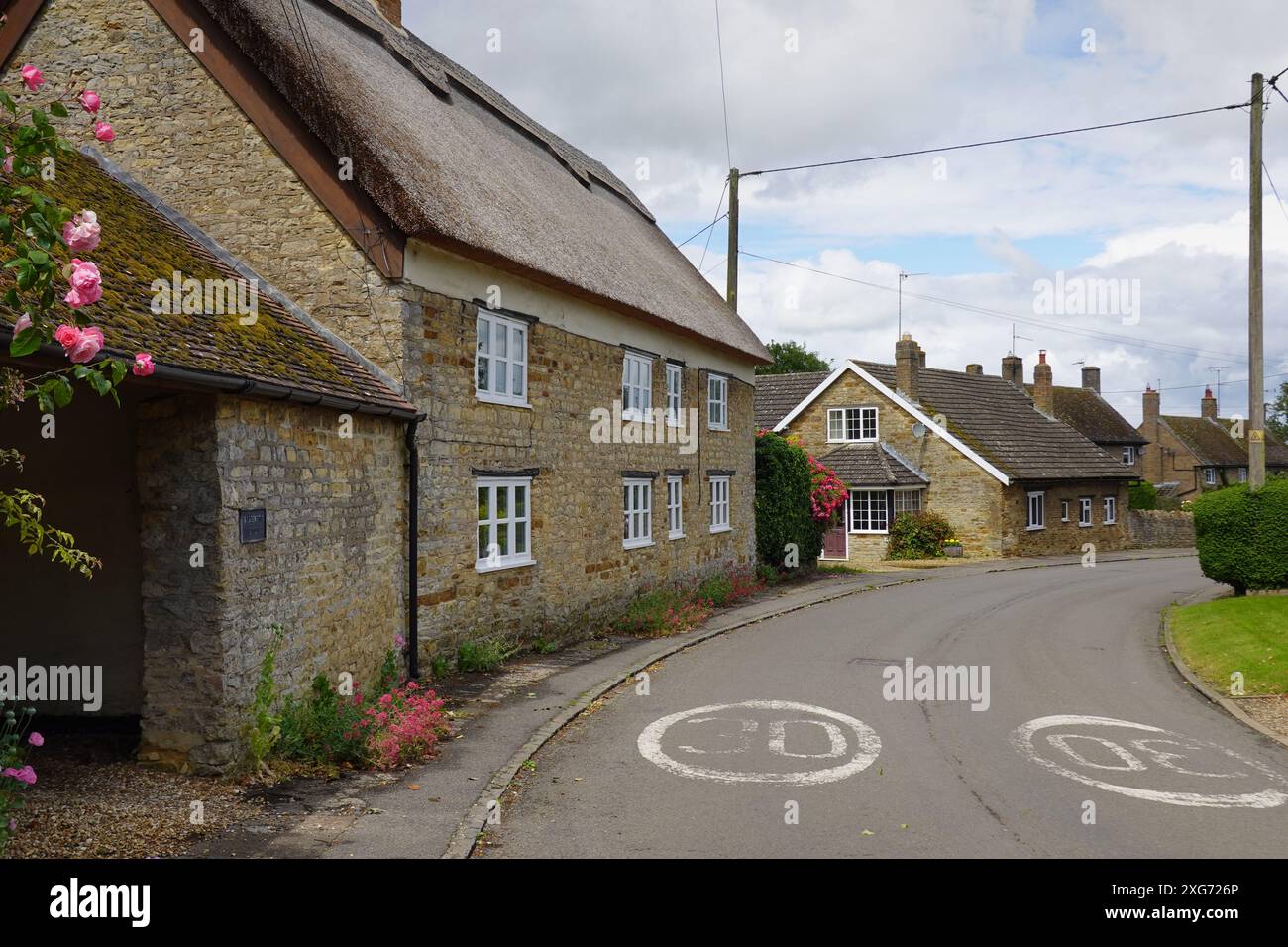 Harrington, Northamptonshire, Inghilterra, Regno Unito - graziosi cottage di paglia nel villaggio di High Street. Pali e fili del telegrafo si estendono dall'altra parte della strada Foto Stock