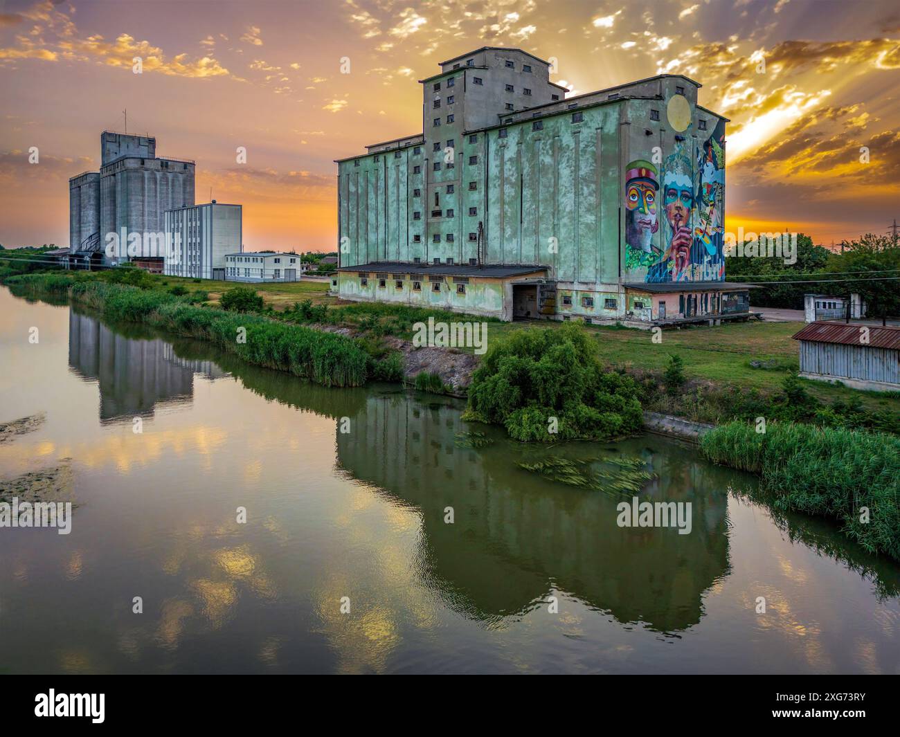 Vecchi silos di cibo sul fiume Bega contro un suggestivo cielo al tramonto. Foto scattata il 30 giugno 2024, Timisoara, Contea di Timis, Romania. Foto Stock