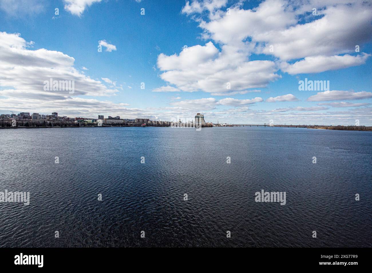 Fiume Dnepr (Dnipro) nella città di Dnipro (ex Ekaterinoslav, Dnepropetrovsk) con vista sul ponte Amursky, hotel incompiuto Parus nella soleggiata giornata di febbraio Foto Stock