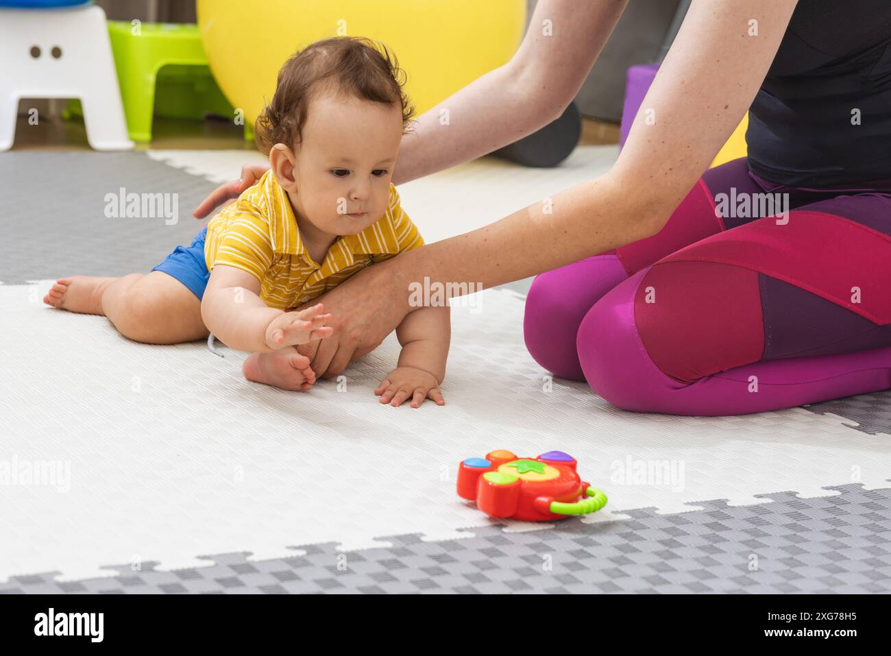 Il fisioterapista aiuta il bambino a strisciare verso un giocattolo durante una sessione di fisioterapia Foto Stock