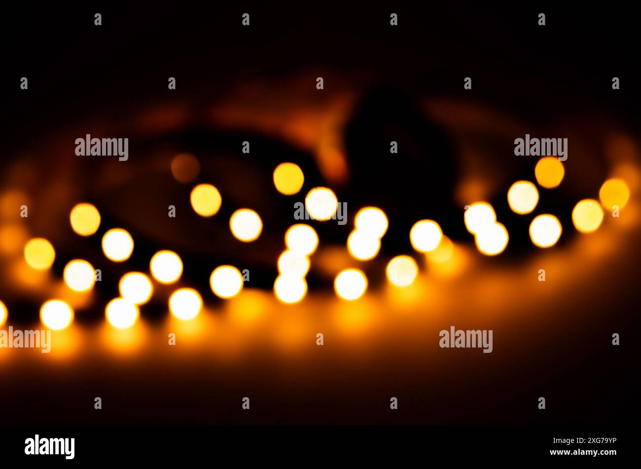 Bokeh notturno su sfondo nero, luci sfocate che creano un'atmosfera festosa di Capodanno e Natale con un bagliore magico e caldo. Foto Stock