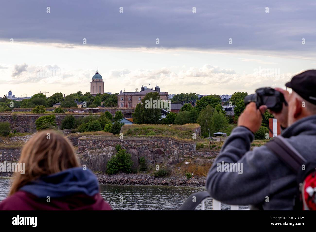 I passeggeri della crociera osservano e fotografano la fortezza marina di Suomenlinna a Helsinki, Finlandia, da un ponte scoperto a bordo. Foto Stock