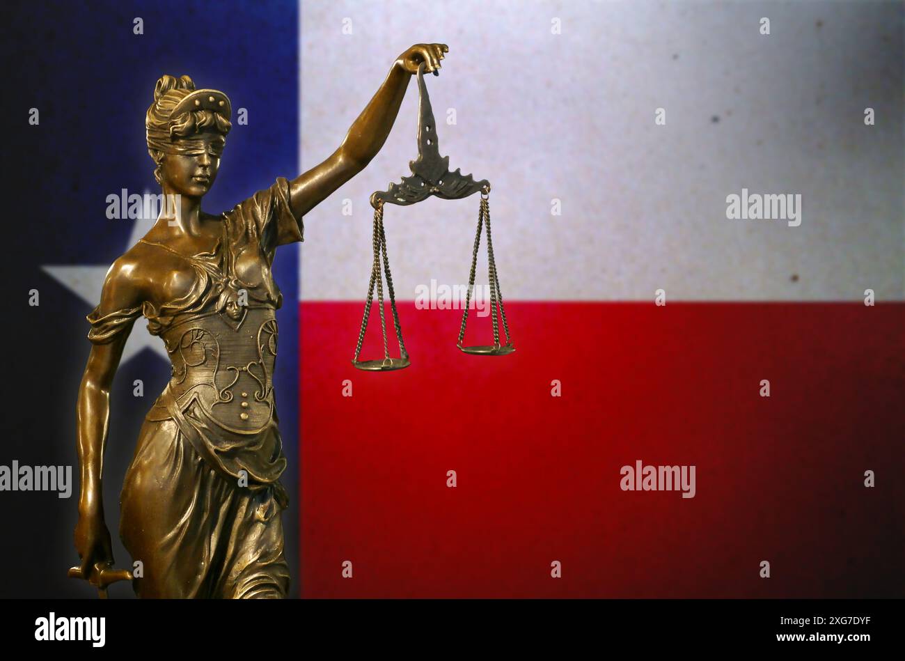 Primo piano di una piccola statuetta di bronzo di Lady Justice davanti a una bandiera del Texas. Foto Stock