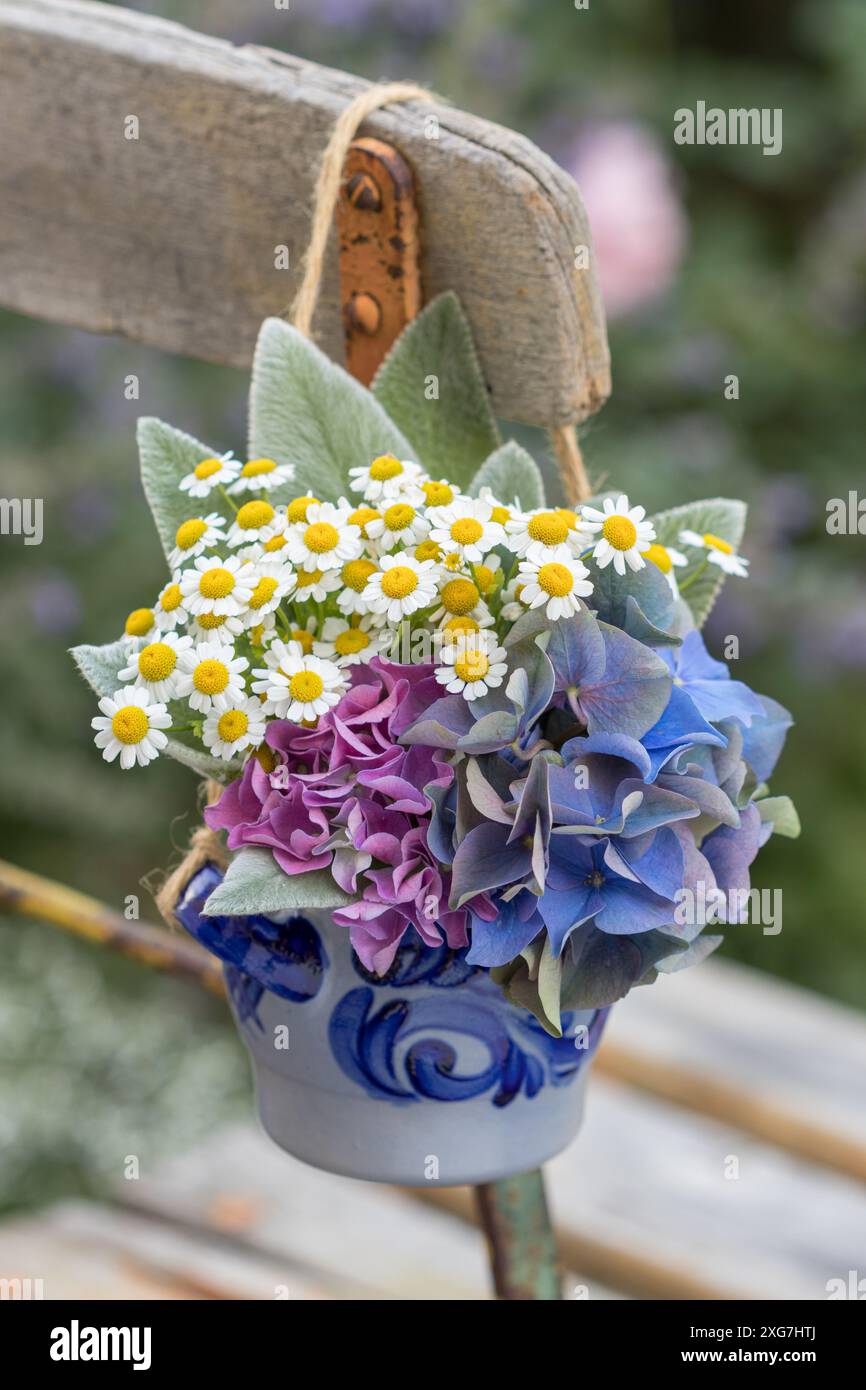 bouquet con ortensie in fiore, feverfew e foglie di agnello in un vaso appeso alla sedia da giardino Foto Stock