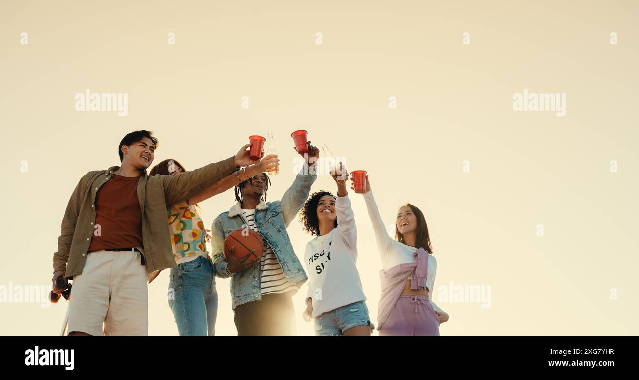 Gruppo di amici felici all'aperto, sorseggiando drink e festeggiando insieme. Divertimento, gioia e amicizia in una giornata di sole. Foto Stock