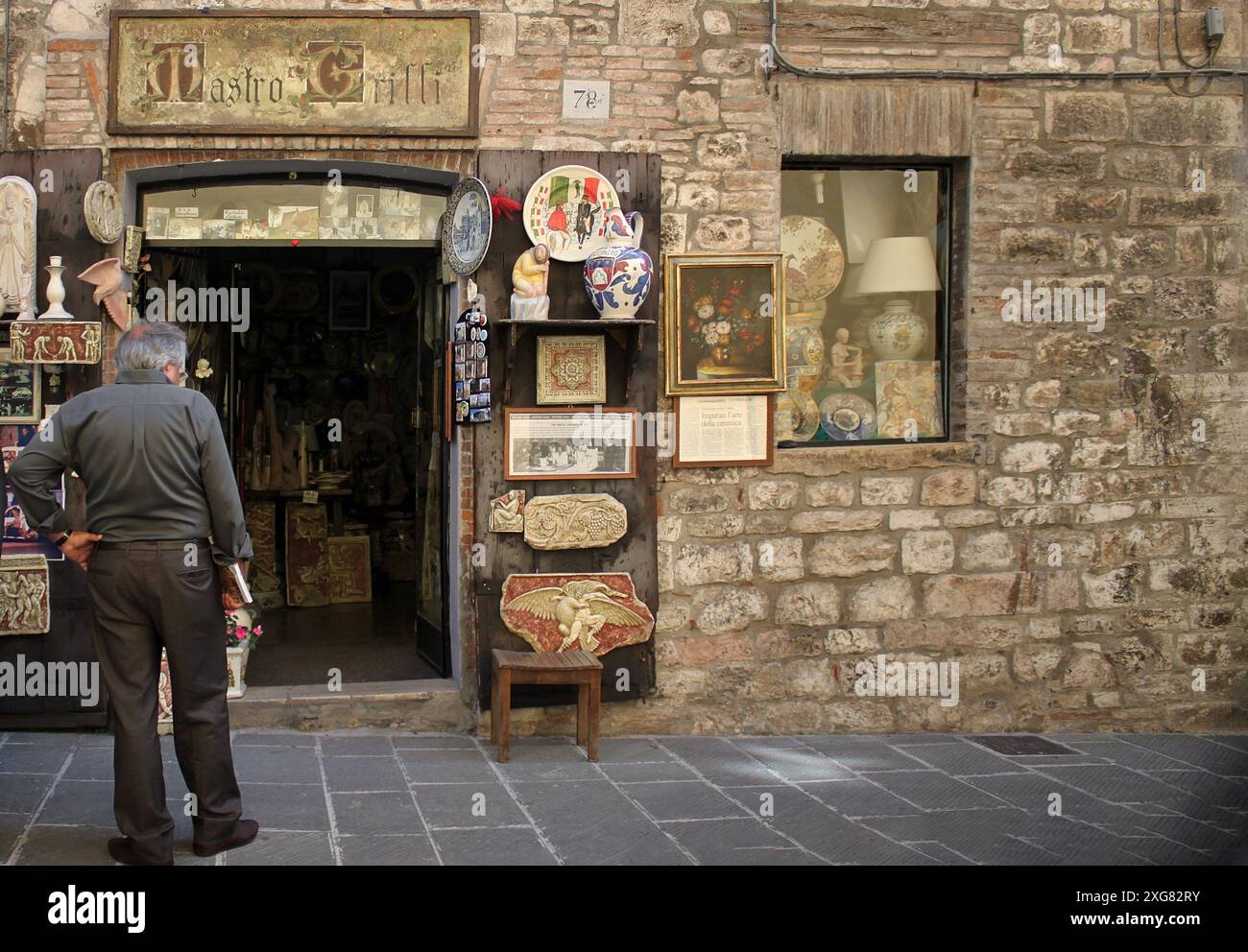 Gubbio, Italia - 3 luglio 2014: Un uomo in piedi di fronte a un negozio di souvenir e d'arte a Gubbio, Umbria, Italia. Foto Stock