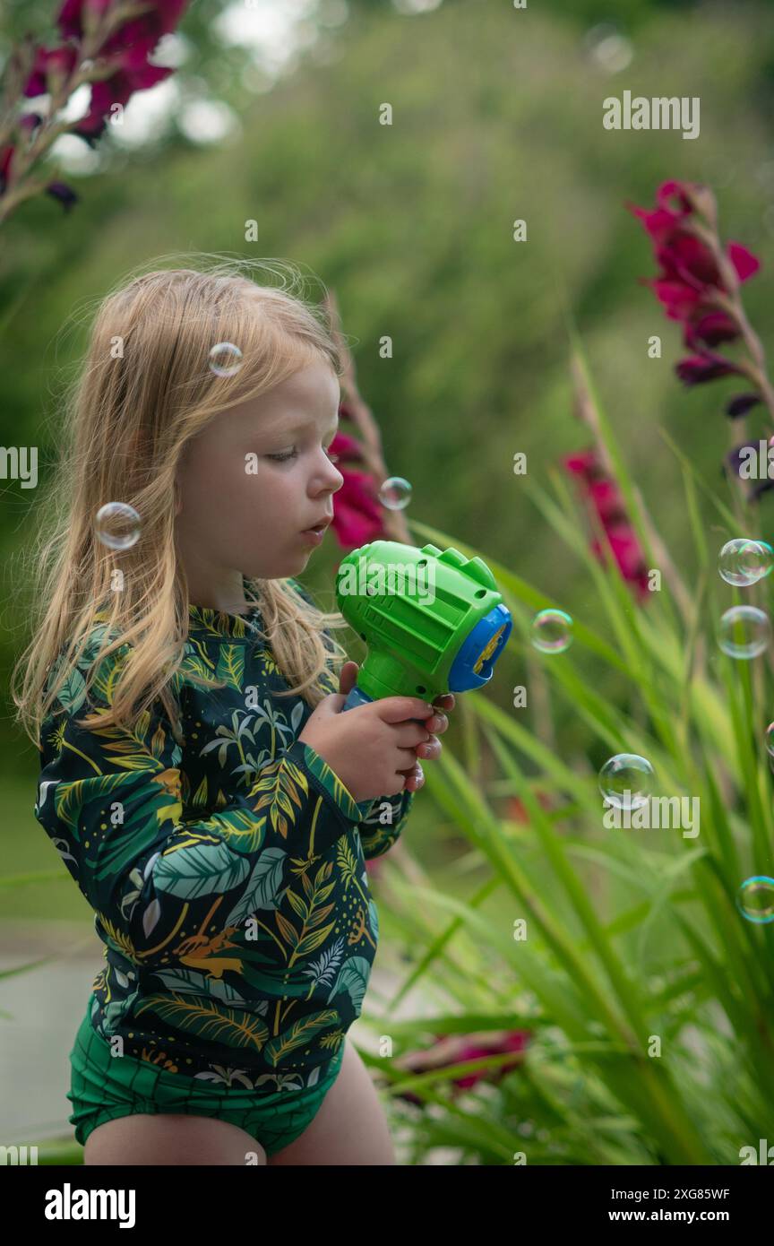 Bambina di tre anni con lunghe bolle bionde che soffiano Foto Stock