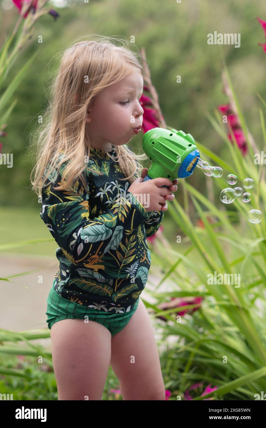 Bambina di tre anni con lunghe bolle bionde che soffiano Foto Stock