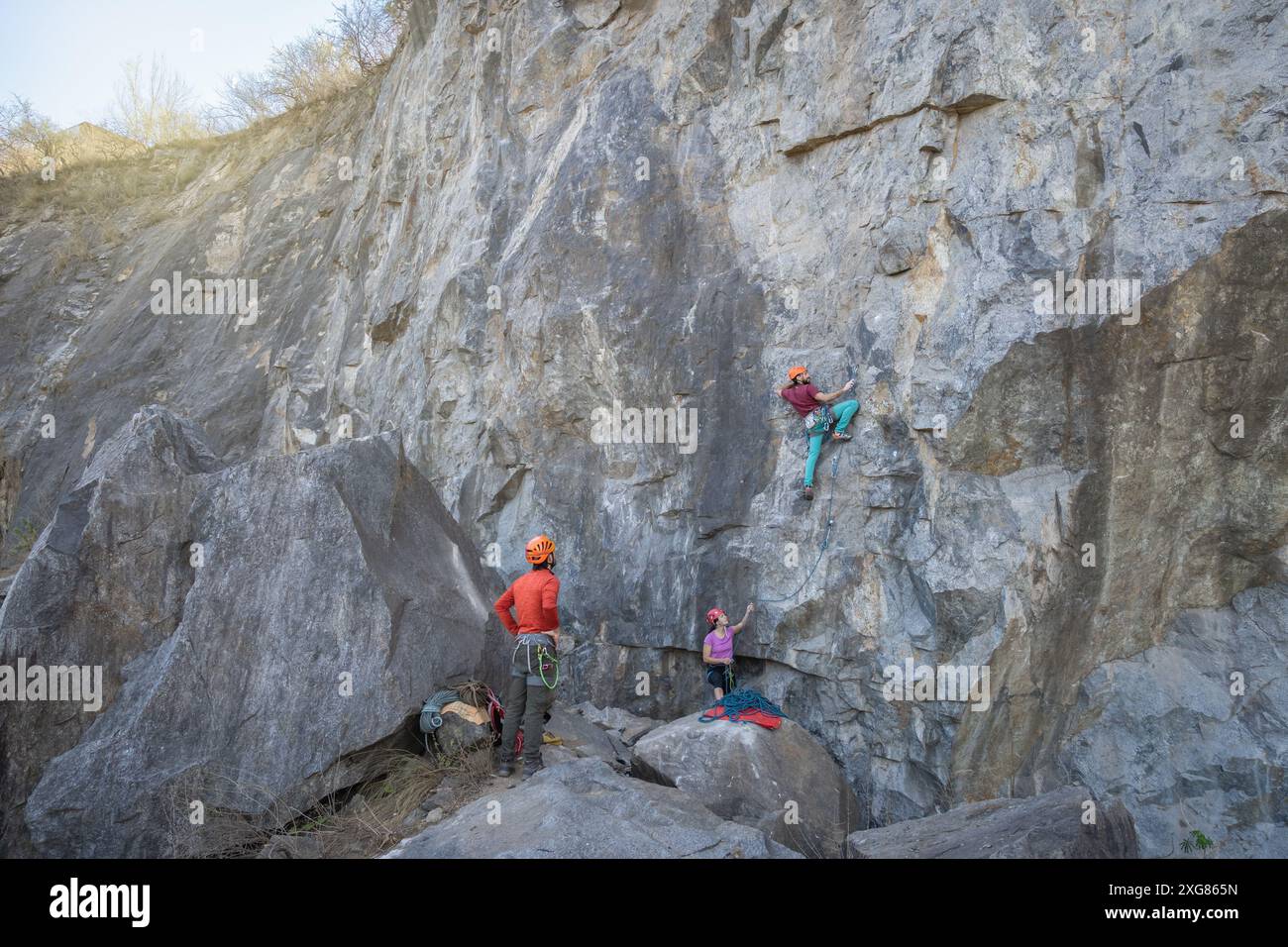 Tre scalatori con zaini salgono su un sentiero roccioso di montagna, mostrando il loro spirito avventuroso e la loro determinazione. Uno di loro indossa un timone arancione Foto Stock