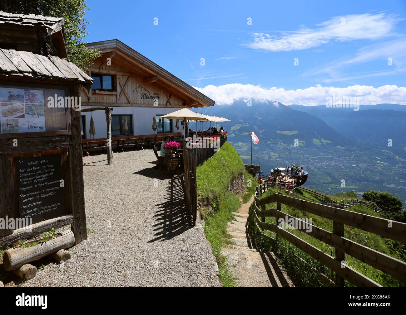 Tirol, Südtirol, Italien 05. Juli 2024: Hier der Blick oberhalb von Dorf Tirol, Tirolo bei Meran auf das Gasthaus Steinegg wo man einkehren kann, Essen, Trinken, ausruhen, hier führt auch der Hans-Frieden- Felsenweg / Meraner Höhenweg, 24 vorbei, unten drunten die Aussichtsplattform, Aussichtskorb Hochmuth, Touchmuth, Texelwen vagabondare, spazieren **** Tirolo, alto Adige, Italia 05 luglio 2024 qui la vista sopra Tirolo, Tirolo vicino a Merano fino alla locanda Steinegg dove ci si può fermare per mangiare, bere, riposare, il Hans Frieden Felsenweg Meraner Höhenweg Foto Stock