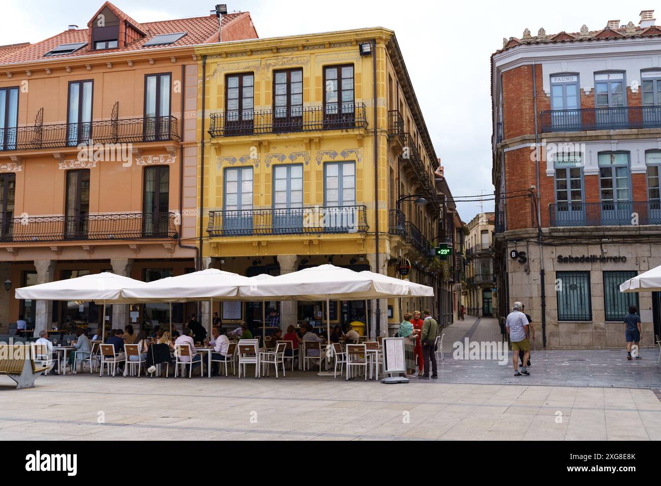 Astorga, Spagna - 4 giugno 2023: Un gruppo di persone sedute ai tavoli all'esterno, con alti edifici che torreggiano sullo sfondo. Foto Stock