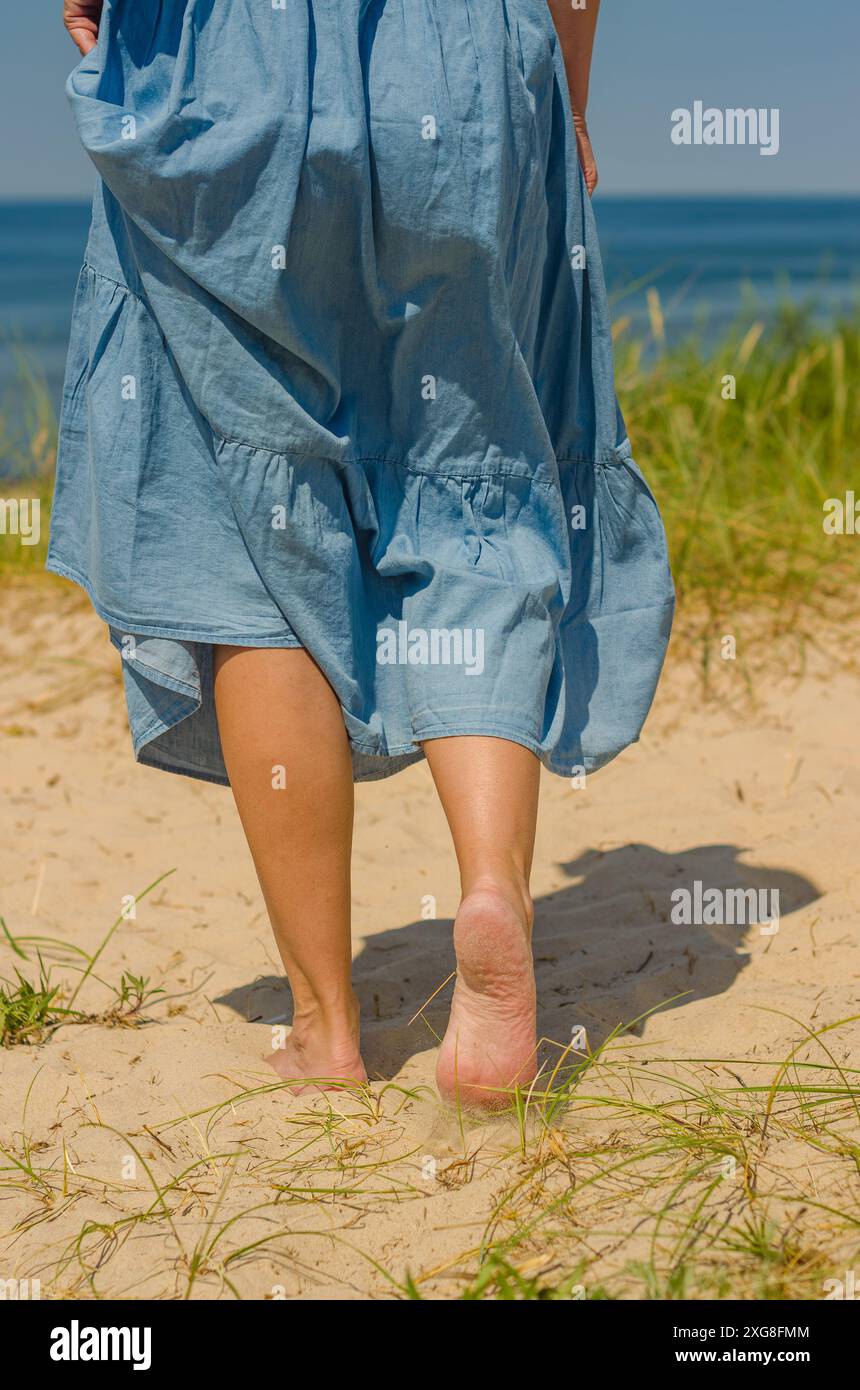 donna gambe in primo piano che cammina su sabbia bianca in spiaggia in abito blu . Foto di alta qualità Foto Stock