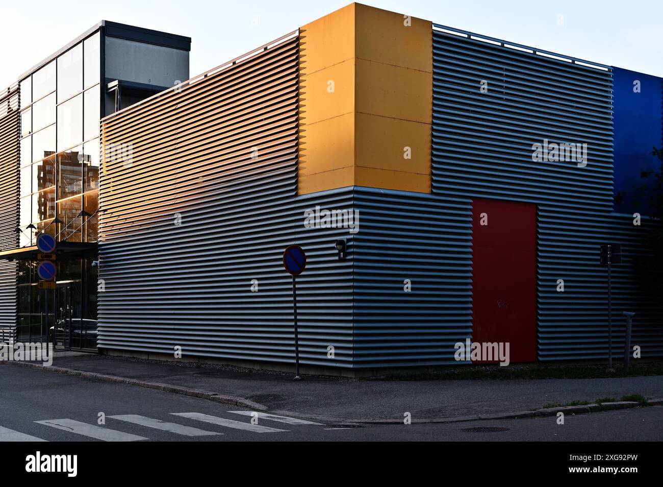Questa immagine mostra un moderno edificio industriale con rivestimenti in metallo ondulato caratterizzati da vibranti pannelli gialli e rossi, che catturano l'essenza del contemporaneo Foto Stock