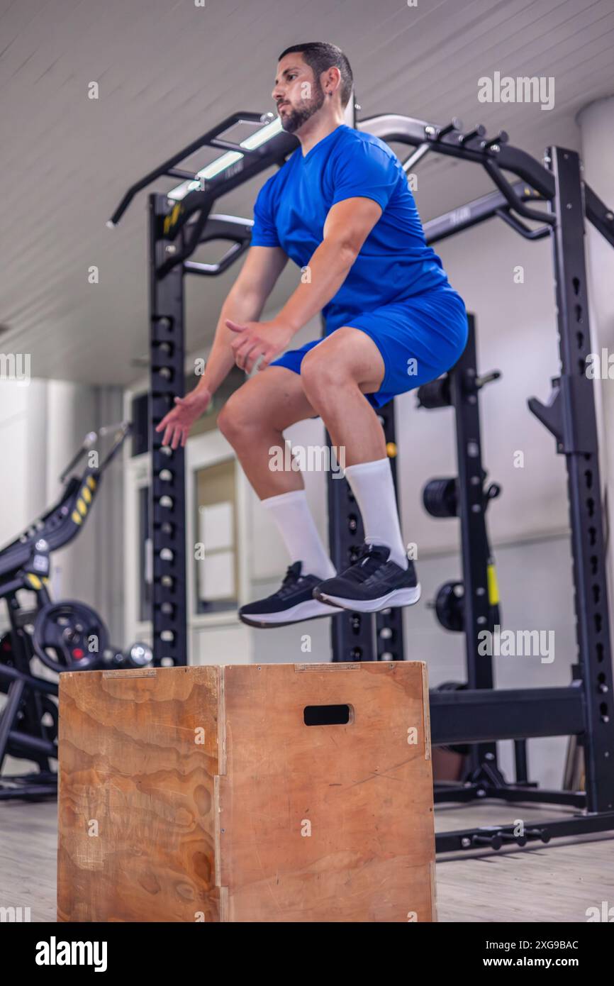 il giovane atleta verticale esegue salti da box durante una sessione in palestra. Questa immagine cattura l'energia e la messa a fuoco necessarie per il plyom ad alta intensità Foto Stock