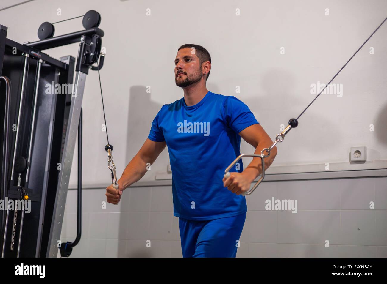 lo sportivo del fitness si vede lavorare i muscoli deltoidi della schiena utilizzando macchine a doppia puleggia in palestra. Questa immagine mostra la dedizione dell'atleta al bui Foto Stock