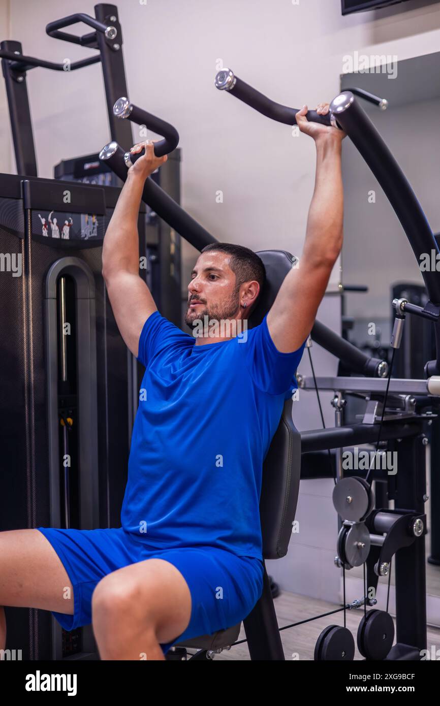 l'atleta di fitness verticale si concentra sull'allenamento dei muscoli delle spalle utilizzando una macchina da palestra durante la sua routine quotidiana di allenamento. Questa immagine cattura il suo dattero Foto Stock l'atleta di fitness verticale si concentra sull'allenamento dei muscoli delle spalle utilizzando una macchina da palestra durante la sua routine quotidiana di allenamento. Questa immagine cattura il suo dattero Foto Stock