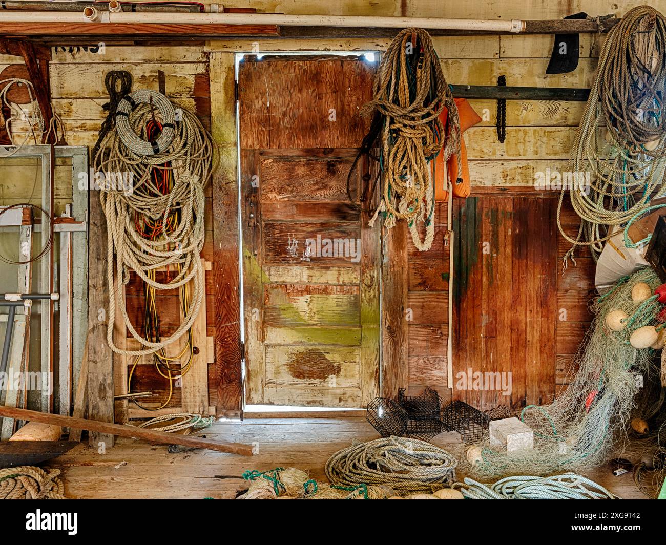 Una porta nel capannone della rete di un allevamento di ostriche conduce all'esterno attraverso un muro pieno di corde e attrezzature per arrivare al molo. Foto Stock
