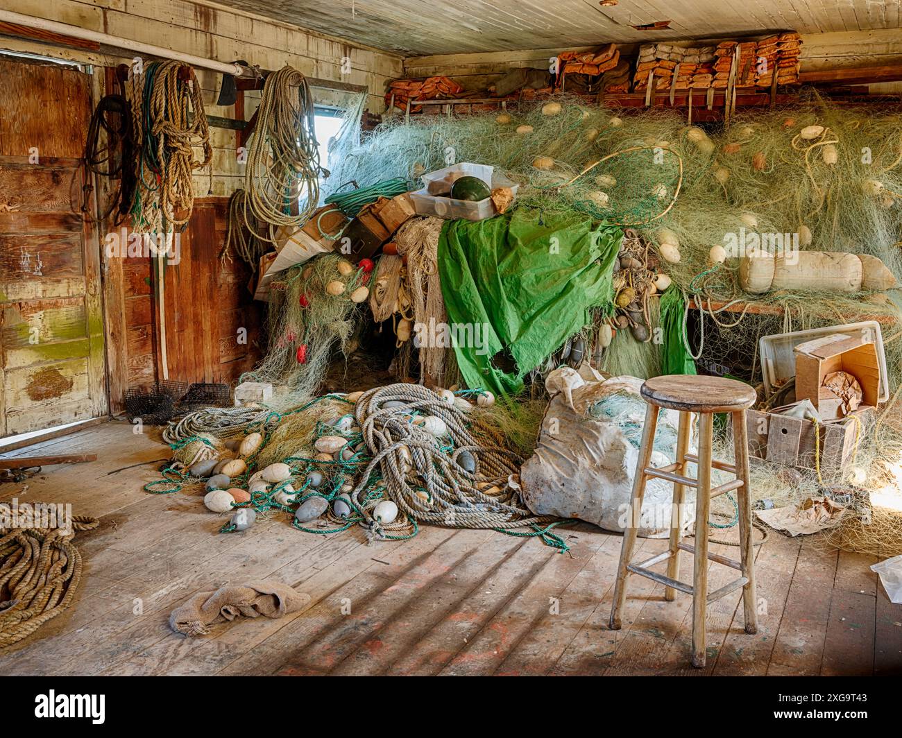 In un angolo del capannone di rete in un allevamento di ostriche, un mucchio di reti da pesca e boe si trovano sul pavimento accanto a un muro. Foto Stock